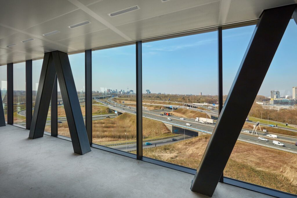Uitzicht vanuit een modern kantoorgebouw aan de Joan Muyskenweg op snelwegen en de skyline van Amsterdam.